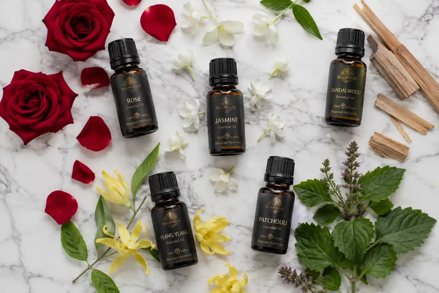 Rose, jasmine, ylang ylang, patchouli, and sandalwood essential oils arranged in amber bottles on a marble surface.