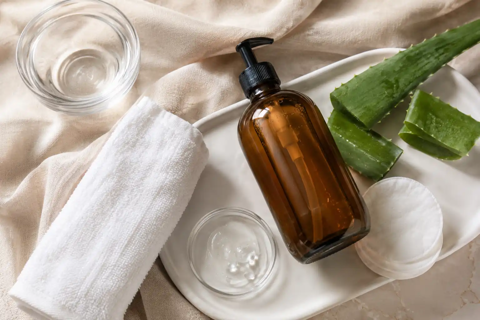 Fragrance-free liquid soap, aloe vera, glycerin, and a clean towel arranged for tattoo aftercare.